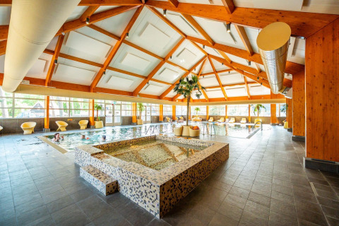 Zona de piscina cubierta con spa, sillones relajantes y estructura de madera en glamping de lujo.
