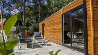 Lodge de bienestar moderno en De Zanding, Países Bajos, con fachada de madera, patio y muebles de exterior.