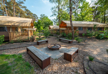 Safari lodgetents with wooden decks and benches around a fire pit in nature at De Zanding, Netherlands.