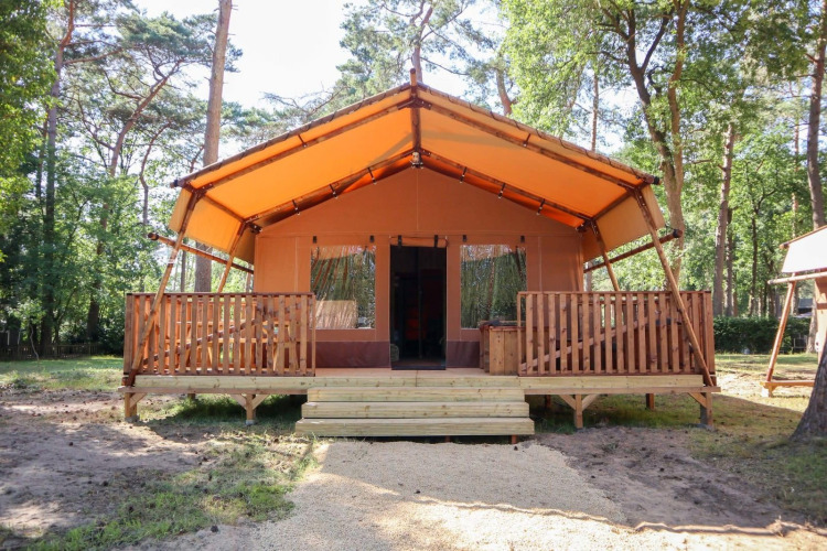 Tienda safari Lodgetent en De Zanding, Países Bajos, rodeada de árboles y con terraza delantera.
