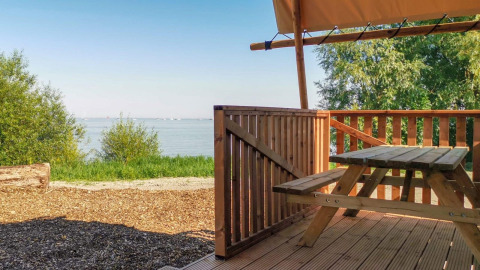 Vue depuis la tente safari Lodgetent à De Zanding, Pays-Bas, terrasse en bois, banc et lac en fond.