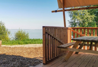 Vue depuis la tente safari Lodgetent à De Zanding, Pays-Bas, terrasse en bois, banc et lac en fond.