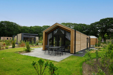 Lodge moderne en bois avec grandes fenêtres et terrasse, située dans un décor forestier verdoyant.