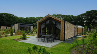 Moderna Forest Lodge con revestimiento de madera y terraza, rodeada de vegetación verde y frondosa.