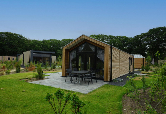Moderna Forest Lodge con revestimiento de madera y terraza, rodeada de vegetación verde y frondosa.