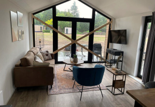 Salon à Forest Lodge à De Zanding, Pays-Bas, avec grandes fenêtres et poutres de bois croisées sur la baie vitrée.