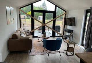 Sala de estar en Forest Lodge en De Zanding, Países Bajos, con grandes ventanales y vigas cruzadas de madera.