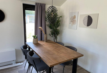 Spisestue i Forest Lodge ved De Zanding i Holland, moderne træbord, grå stole og kunstværker på væggen.