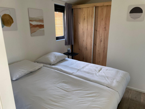 Dormitorio en Forest Lodge en De Zanding, Países Bajos, con cama doble, armario de madera y arte en la pared.