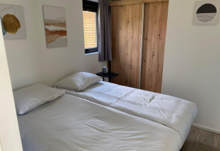 Dormitorio en Forest Lodge en De Zanding, Países Bajos, con cama doble, armario de madera y arte en la pared.