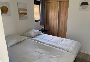 Dormitorio en Forest Lodge en De Zanding, Países Bajos, con cama doble, armario de madera y arte en la pared.