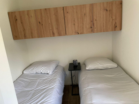 Dos camas individuales con sábanas blancas, una mesa pequeña y armarios de madera en Forest Lodge, De Zanding.