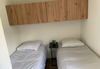 Dos camas individuales con sábanas blancas, una mesa pequeña y armarios de madera en Forest Lodge, De Zanding.