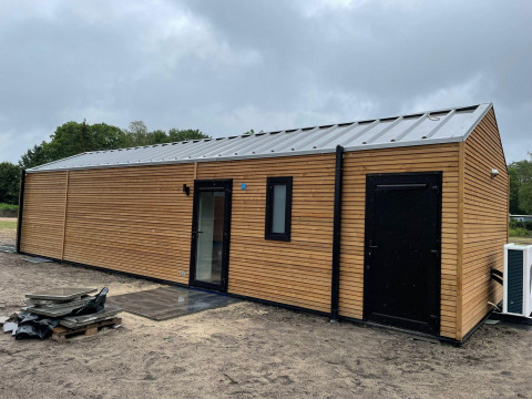 Foto della Forest Lodge a De Zanding nei Paesi Bassi, con una moderna casetta di legno sotto cielo nuvoloso.