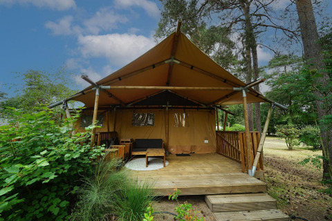 Safari tent Lodgetent with wooden deck, set in a peaceful forest area surrounded by lush greenery.