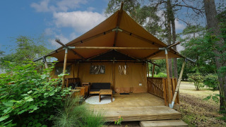 Safari-Zelt Lodgetent mit Holzterrasse im Wald, umgeben von Bäumen und grüner Vegetation.