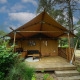 Tenda safari Lodgetent con veranda in legno immersa in un bosco ricco di alberi e vegetazione.