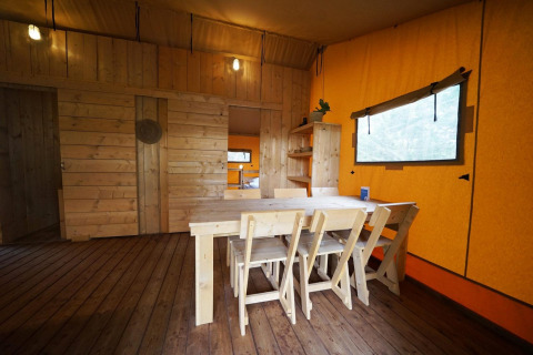 Essbereich mit Holzmöbeln im Safarizelt Lodgetent bei De Zanding, Niederlande, mit orangen Wänden.