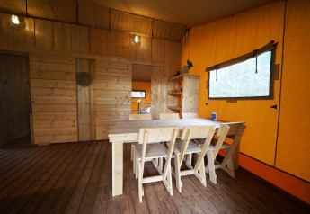 Træmøbleret spiseområde i en safaritelts-lodge ved De Zanding, Holland, med naturtræ og orange vægge.