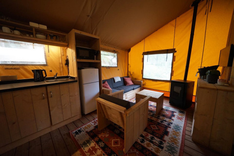 Hyggeligt interiør i en Lodgetent på De Zanding, Holland, med køkken, sofa, træmøbler og brændeovn.