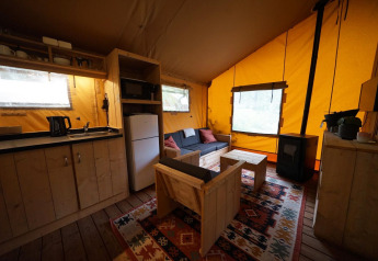 Intérieur douillet de la Lodgetent à De Zanding, Pays-Bas, avec coin cuisine, canapé et poêle à bois.