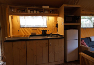 Kitchen area inside a Lodgetent safari tent at De Zanding in the Netherlands, with fridge and utensils.
