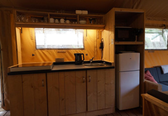 Küchenbereich im Safarizelt Lodgetent bei De Zanding, Niederlande, mit Kühlschrank und Geschirr.