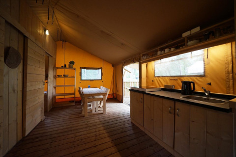 Interior view of a safari tent lodge at De Zanding in the Netherlands, featuring wood furniture and kitchen.