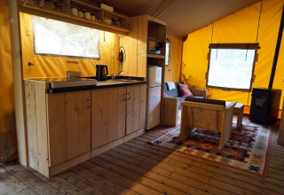 Interior de tienda safari Lodgetent en De Zanding, Países Bajos, con muebles de madera y cocina.