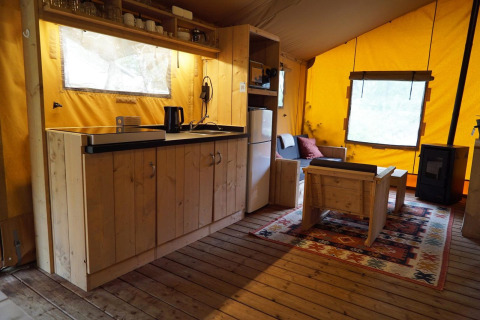 Interior de tienda safari Lodgetent en De Zanding, Países Bajos, con muebles de madera y cocina.