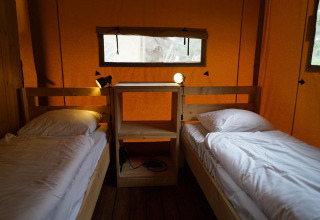 Interior de una tienda safari Lodgetent en De Zanding, Países Bajos, con dos camas y estantería de madera.