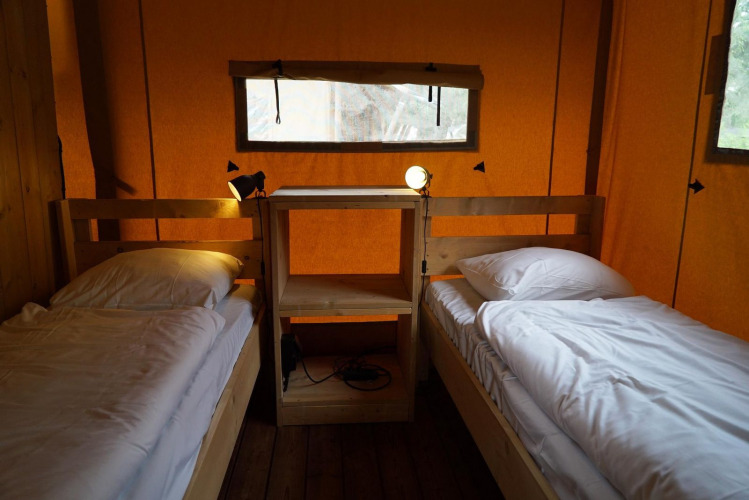 Interior de una tienda safari Lodgetent en De Zanding, Países Bajos, con dos camas y estantería de madera.