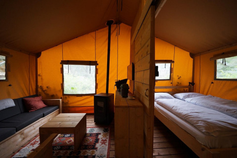 Indvendig udsigt af en lodgetelt på De Zanding i Holland, med seng, sofa, bord og trævæg.