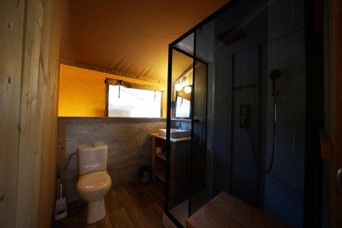 Safari tent bathroom at Lodgetent De Zanding, Netherlands, featuring a toilet, shower, and sink area.