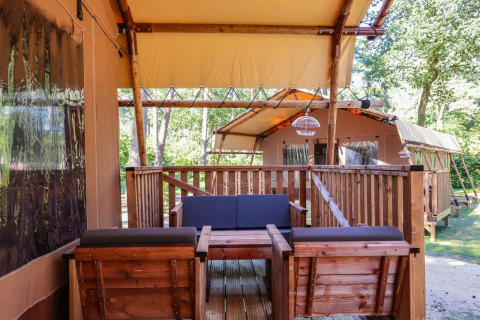 Safari tents with wooden furniture on a deck at Lodgetent, De Zanding in the Netherlands, surrounded by trees.