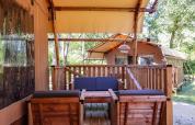 Tiendas safari con muebles de madera en una terraza en Lodgetent de De Zanding, Países Bajos, entre árboles.