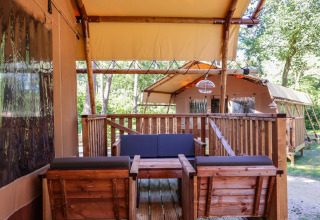 Safari tents with wooden furniture on a deck at Lodgetent, De Zanding in the Netherlands, surrounded by trees.