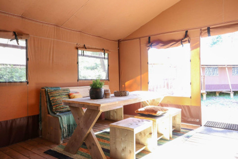 Interior de una tienda safari con mesa y banco de madera en Lodgetent De Zanding, Países Bajos.