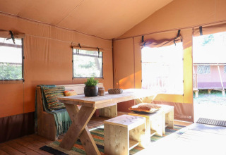 Interior de una tienda safari con mesa y banco de madera en Lodgetent De Zanding, Países Bajos.