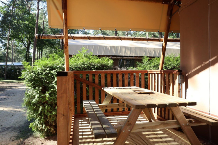 Outdoor terrace with wooden table and benches at Lodgetent safari tent at De Zanding in the Netherlands.
