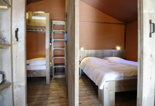 Interior de una tienda safari Lodgetent en De Zanding, Países Bajos, con litera y cama doble de madera.