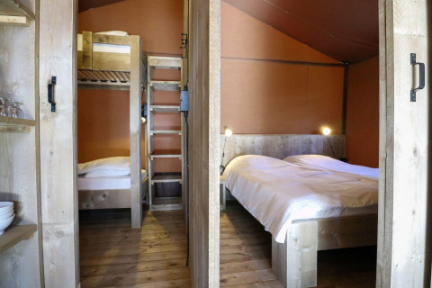 Interior de una tienda safari Lodgetent en De Zanding, Países Bajos, con litera y cama doble de madera.