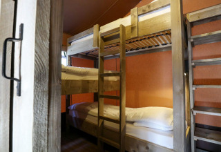 Innenaufnahme mit Etagenbetten in einem Lodgetent bei De Zanding, Niederlande, mit Holzrahmen und orangen Wänden.