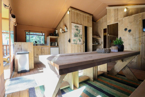 Interior de la tienda safari Lodgetent en De Zanding, Países Bajos, con muebles rústicos de madera.