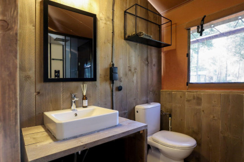 Badeværelse med trævægge, hvid vask, spejl og toilet i en safariteltsuite på De Zanding, Holland.