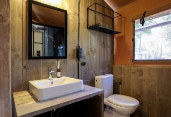 Badeværelse med trævægge, hvid vask, spejl og toilet i en safariteltsuite på De Zanding, Holland.