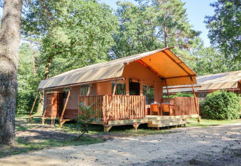 Tienda de safari llamada Lodgetent en De Zanding, Países Bajos, rodeada de árboles y naturaleza en un día soleado.