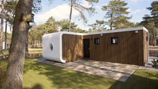 Modus L-Lodge mit moderner Holzverkleidung und weißen Elementen im Wald, sonniger Außenbereich.