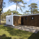 Modus L-lodge med moderne træfacade og hvidt hjørne, omgivet af fyrretræer og solrigt udeområde.