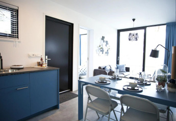 Moderne lodge Modus L ved De Zanding i Holland med åbent køkken, spisebord og stue i blå nuancer.